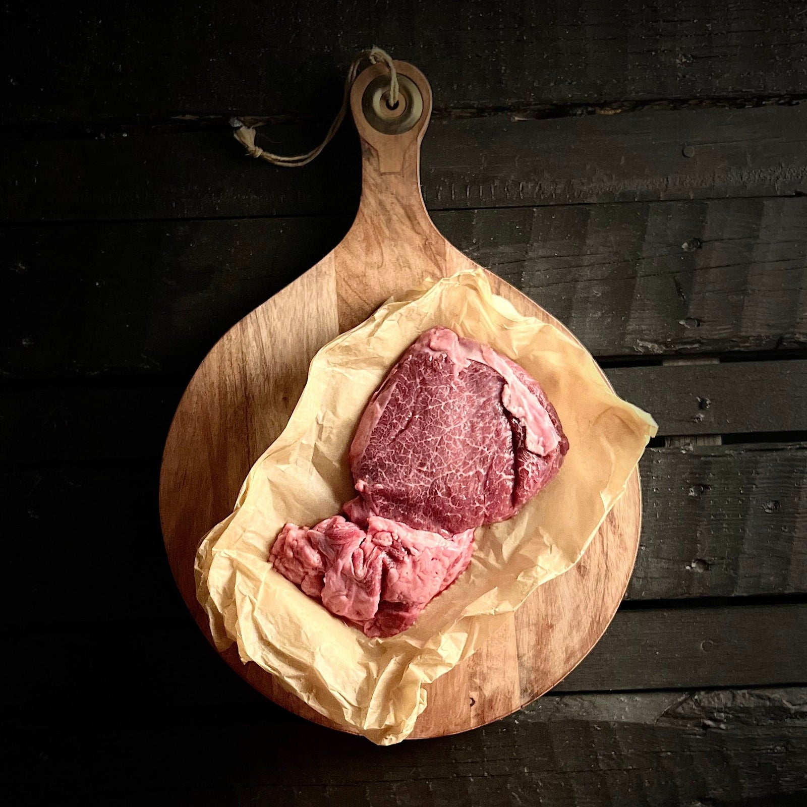 Raw cheek meat on open paper wrapping atop round cutting board