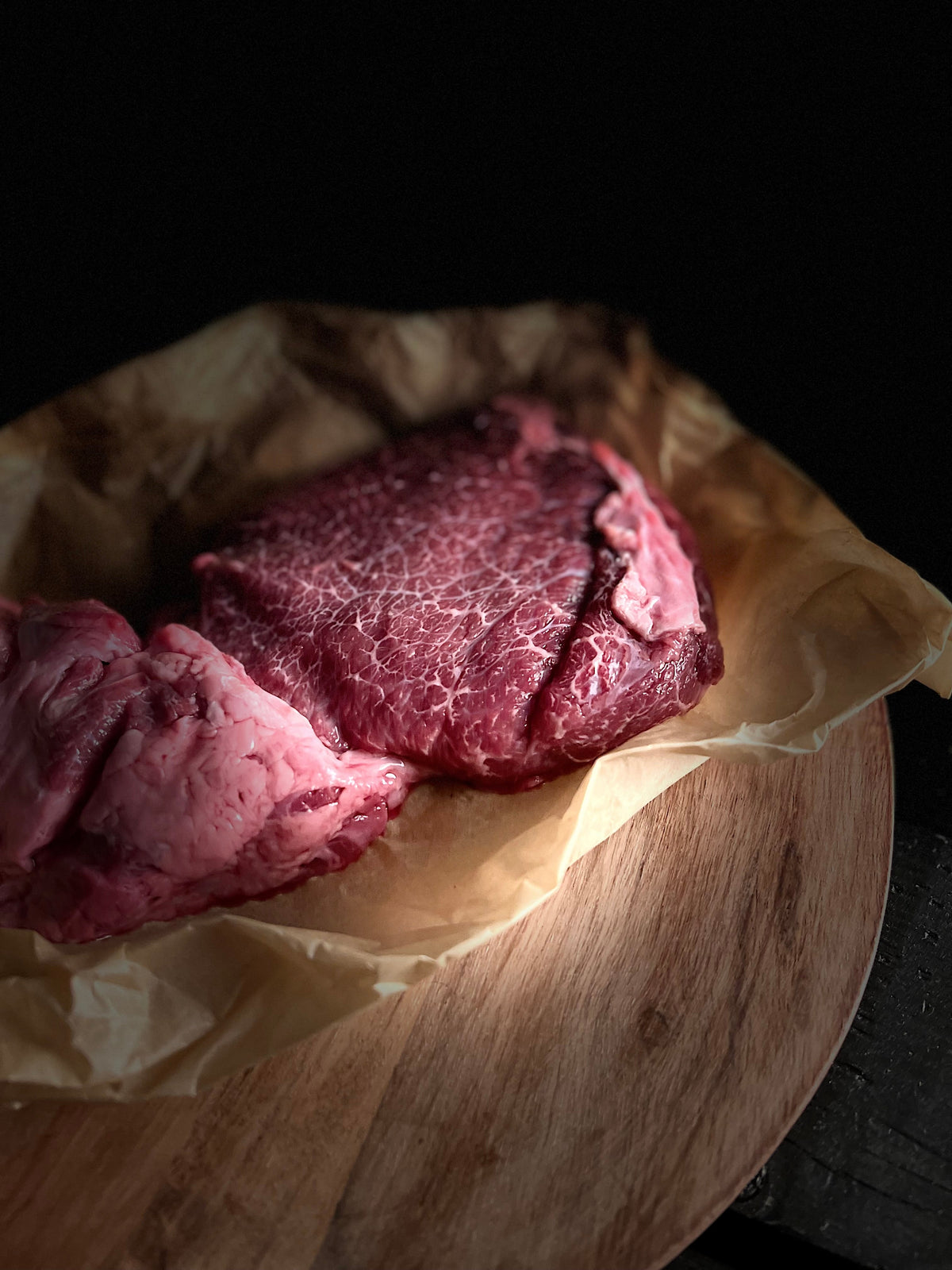 Close up shot of raw cheek meat on open wrap paper atop cutting board