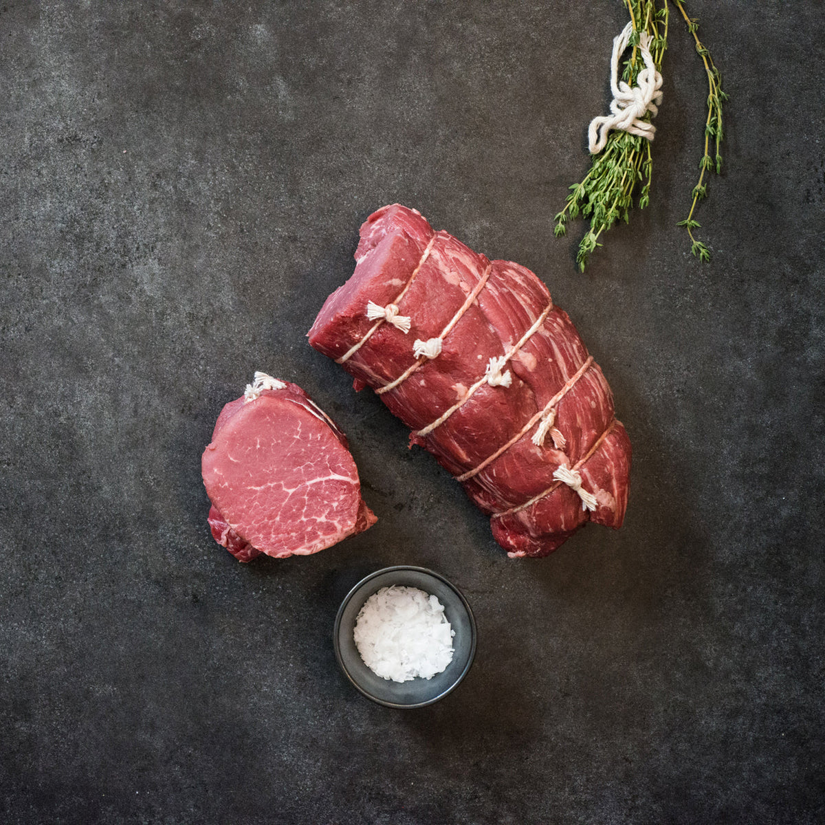 cut filet mignon steak next to whole filet, garnish, and salt on slab