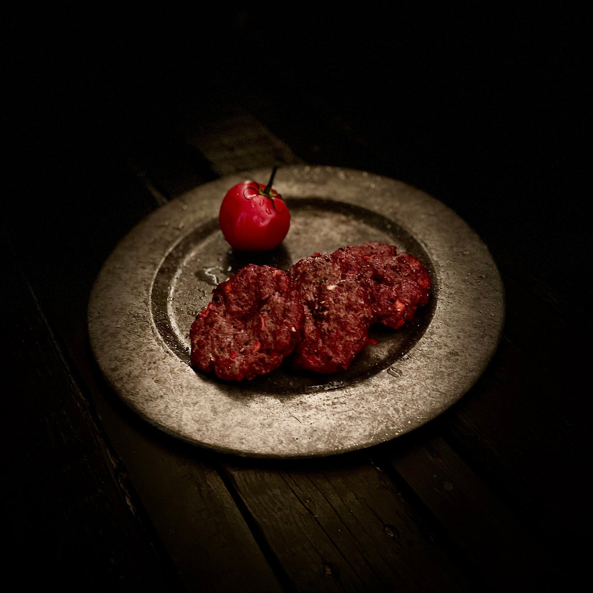 3 cooked beef patties and small whole tomato on round plate