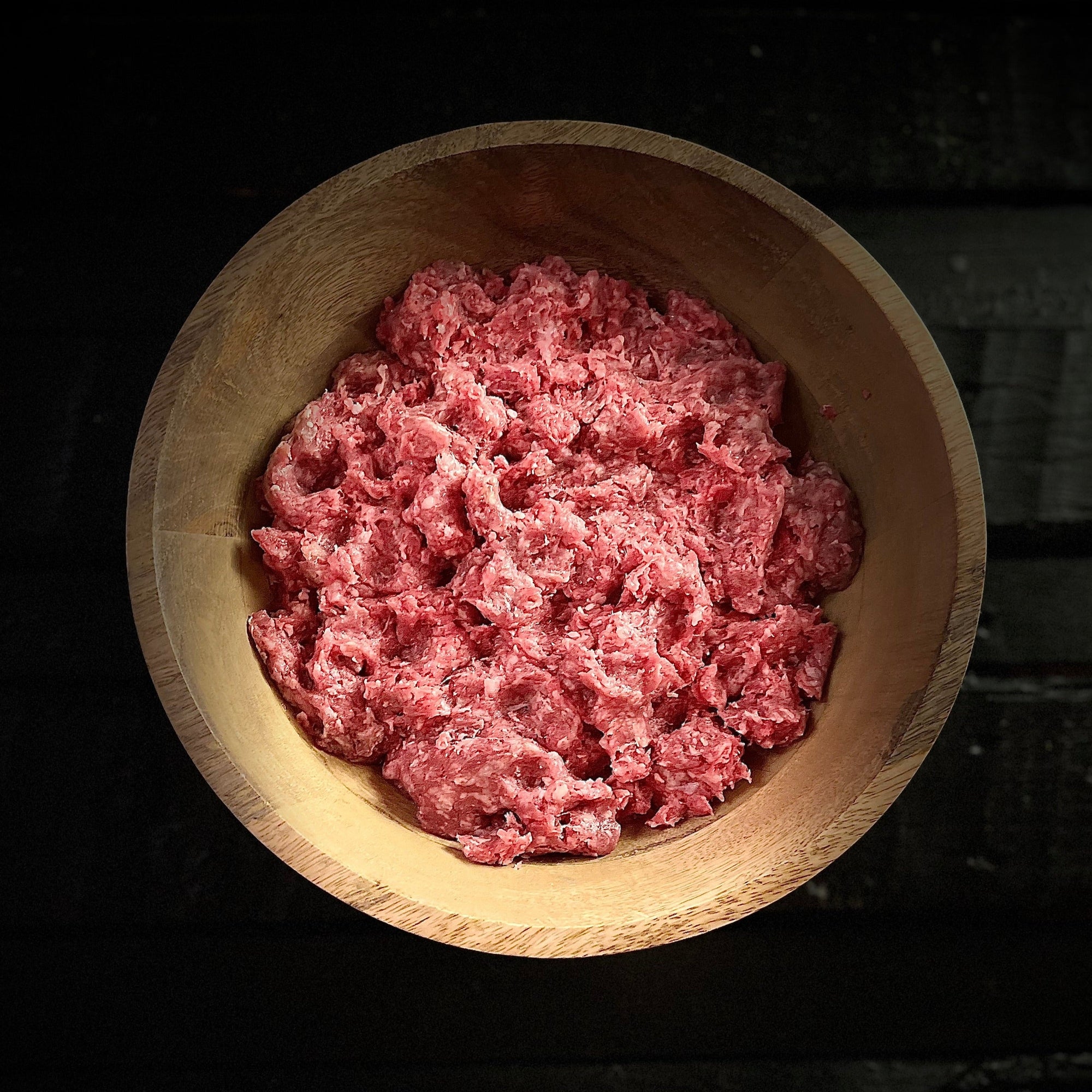 Raw ground beef spread out in wood bowl on slab