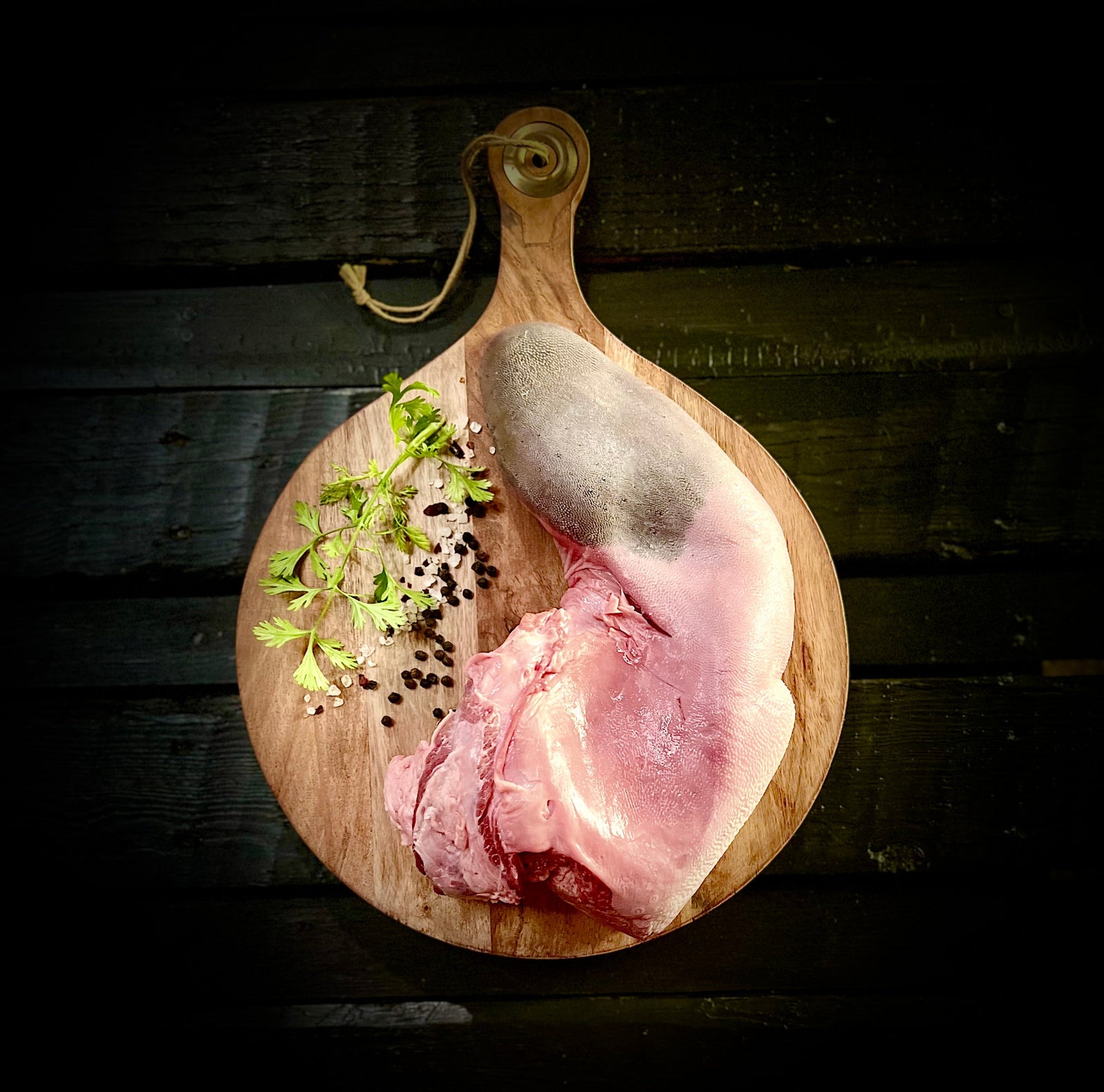 Raw beef tongue and herbs on a round cutting board